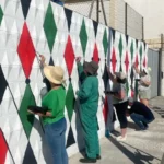 Miembros de La Máquina Creativa y Puerto Real por Palestina pintando un segundo mural con los colores de la bandera.