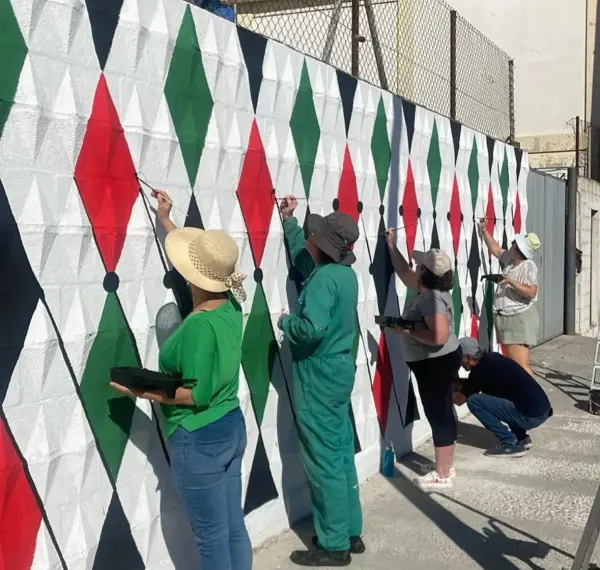 Miembros de La Máquina Creativa y Puerto Real por Palestina pintando un segundo mural con los colores de la bandera.